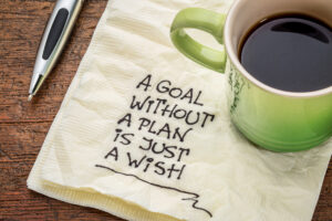 A coffee cup, a pen, and a napkin with the words "A goal without plan is just wish" written on it