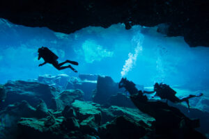 Scuba divers swimming through an underwater cave