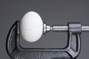 An egg in a C-clamp, cracking from the pressure.