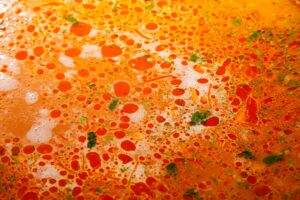Surface of vegetable soup with drops of fat and herbs.
