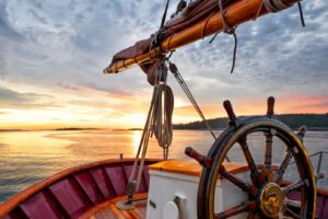 Close up of a sailing ship's steering wheel, bow and boom against a dramatic sky at dawn