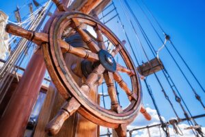 A wooden steering wheel on the deck of a sailing ship